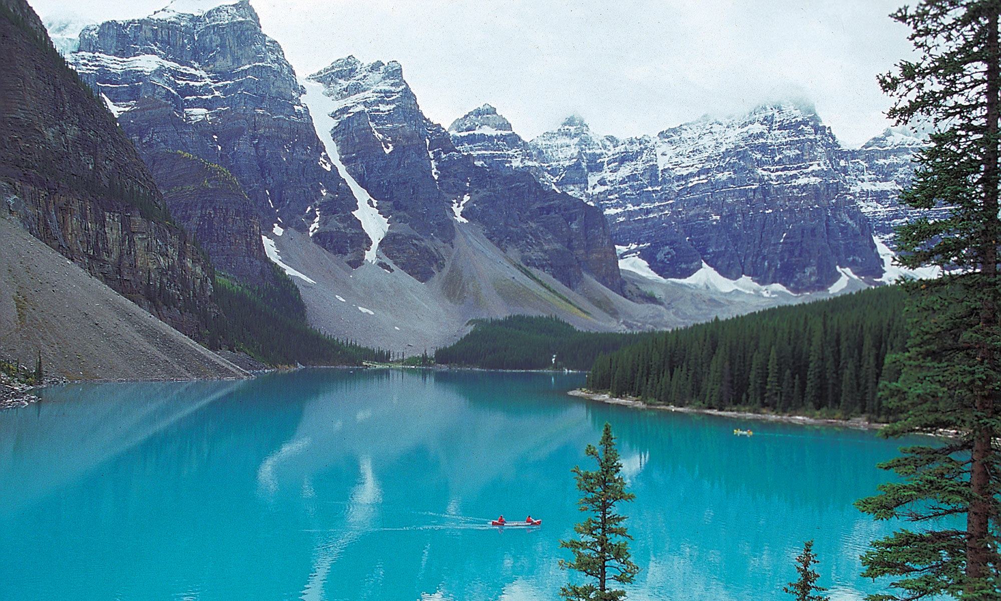 Single canoe in a serene lake surrounded by snowy mountains and forest