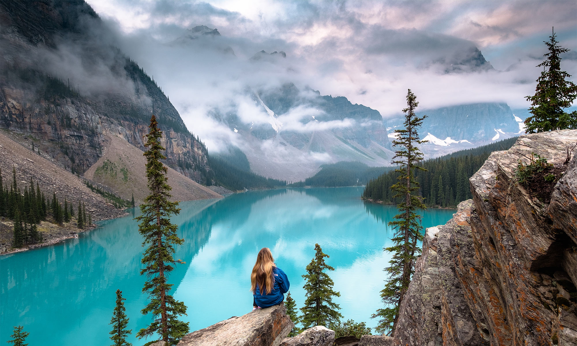 Woman sitting on rock overlooking majestic Moraine Lake in summer