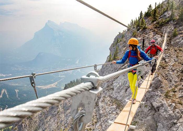Girl and guy walking along a thin plank rope bridge across mountain tops