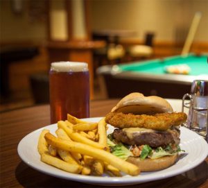 specialty burger with fries and a pint with a pool table in background