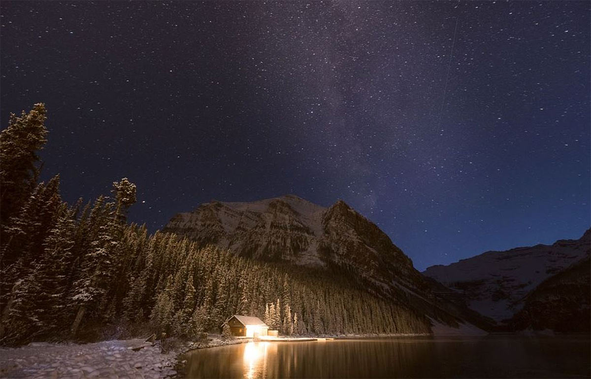 A cabin with the lights by a lake on a clear starry night,