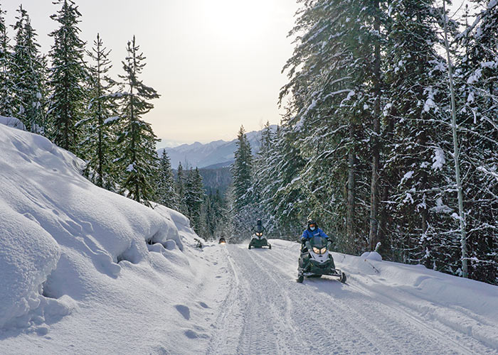 Snow mobiling on snowy road through forest with mountains views