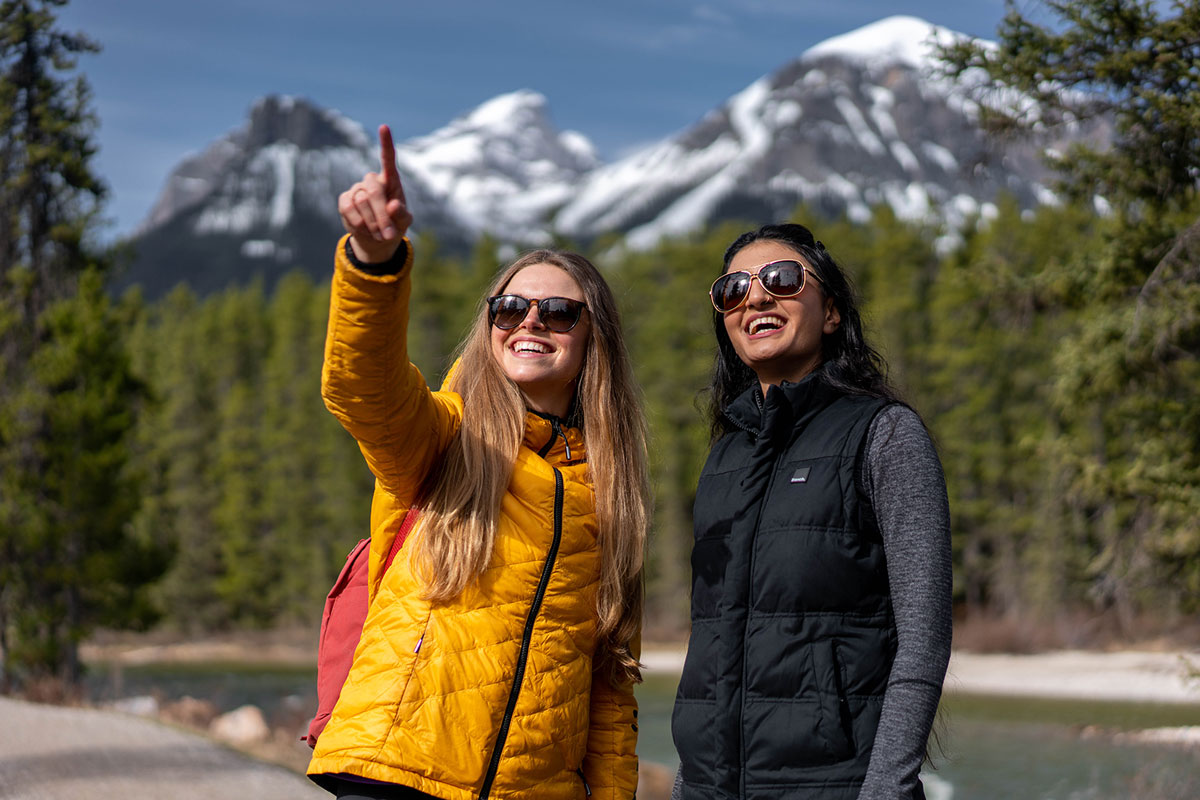 person pointing out something to friend surrounded by trees and mountains on a sunny day