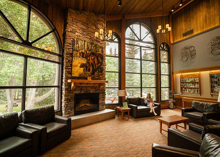 Lake Louise Inn lobby with high ceilings, tall windows, and a woman reading a book.