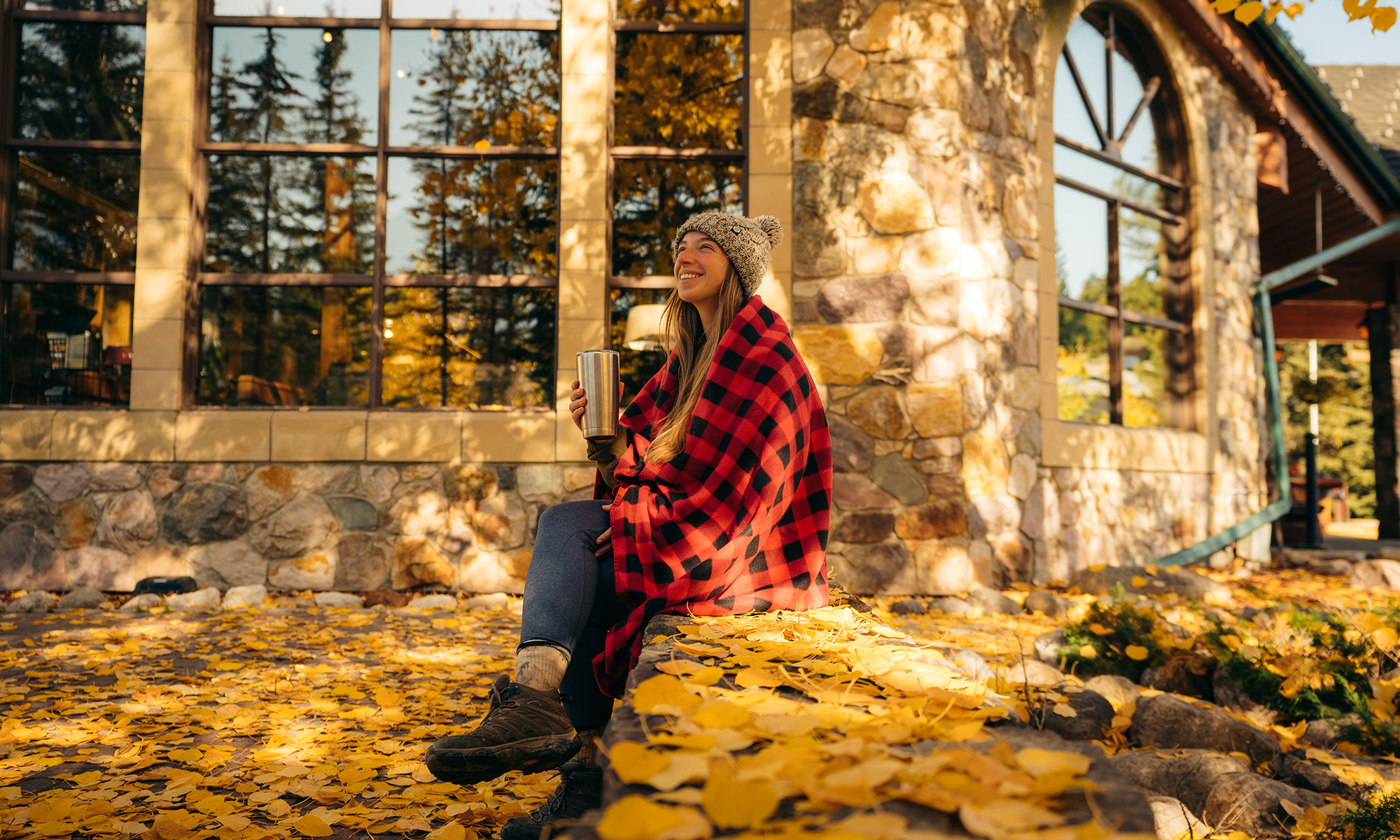 Woman sitting down with a coffee mug outside Lake Louise Inn, surrounded by Fall foliage and colours