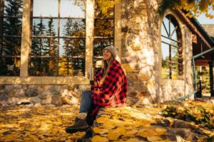 Woman sitting down with a coffee mug outside Lake Louise Inn, surrounded by Fall foliage and colours